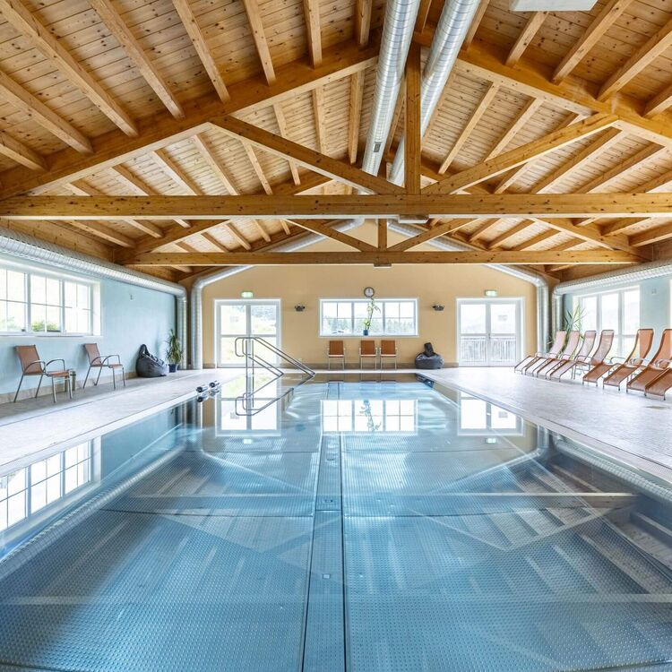 Großzügiges Hallenbad im Resort mit Schwimmbecken, Holzdecke, Panoramafenstern und Liegestühlen für entspannte Stunden