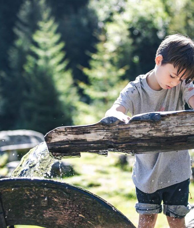 A child examines a wooden water wheel.
