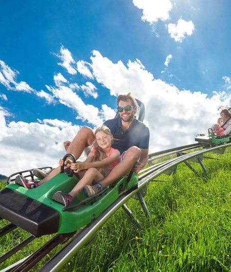 A family races downhill in two cars on the Alpine Coaster Maisiflitzer.