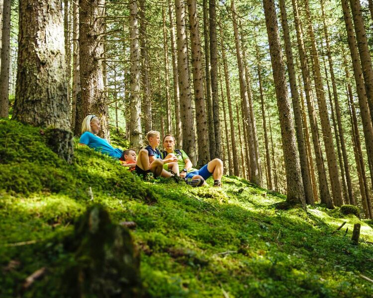 Eltern machen mit ihren 2 Kindern Rast am bemoosten Waldboden © TVB Rauris