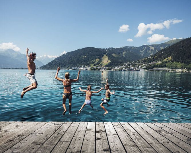 Familie springt in den Zeller See, im Hintergrund das Kitzsteinhorn und die Stadt Zell am See.