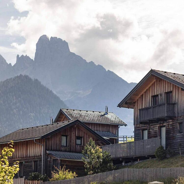 Drei Ferienhäuser im alpinen Stil vor der markanten Bergkulisse des Salzburger Landes