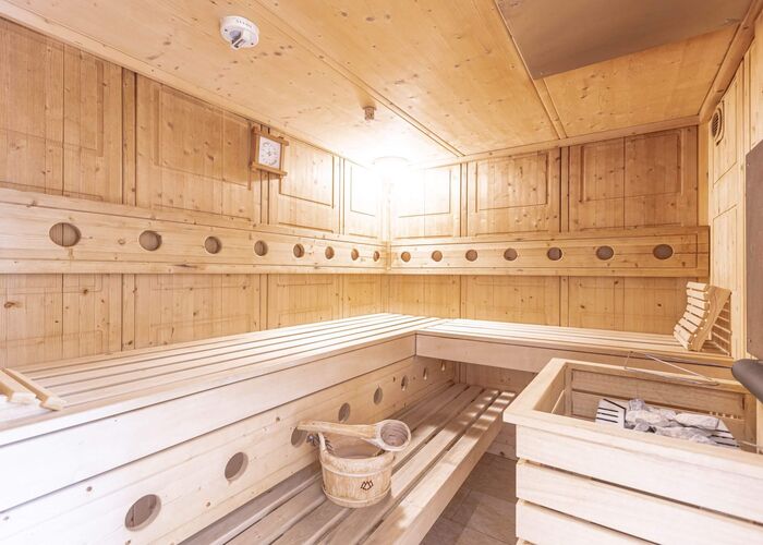Gemütliche Sauna im Ferienhaus mit hellem Holz, breiten Holzbänken, Saunaofen mit Steinen und Holzkübel