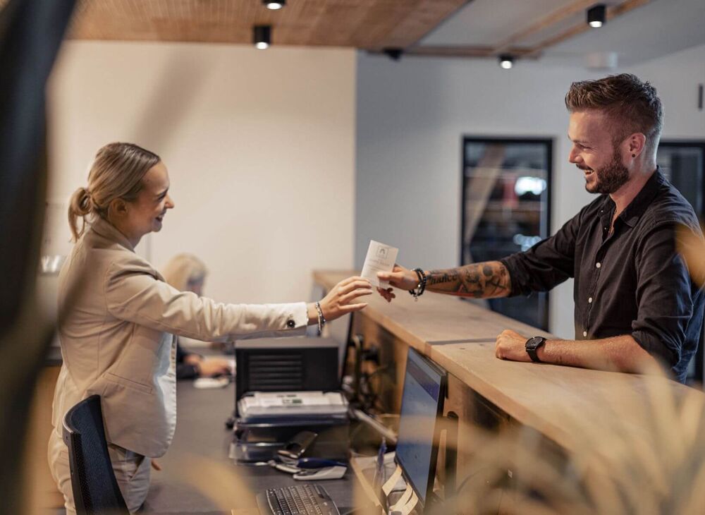 A receptionist hands her guest a guest card.