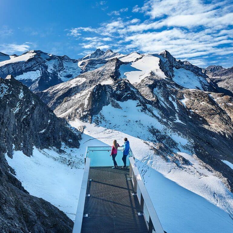 Pärchen blickt von einer Panoramaplattform auf den Großglockner und weitere 3.000er der Hohen Tauern.