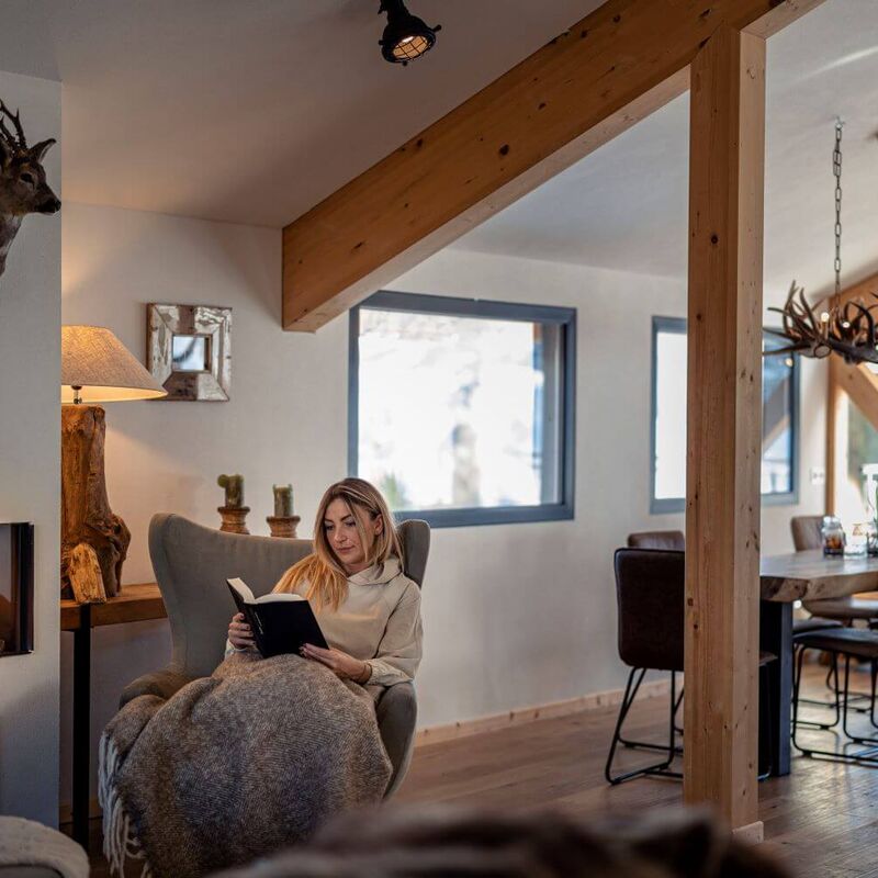 Eine Frau sitzt mit einem Buch vorm Kamin in ihrem Ferienhaus.