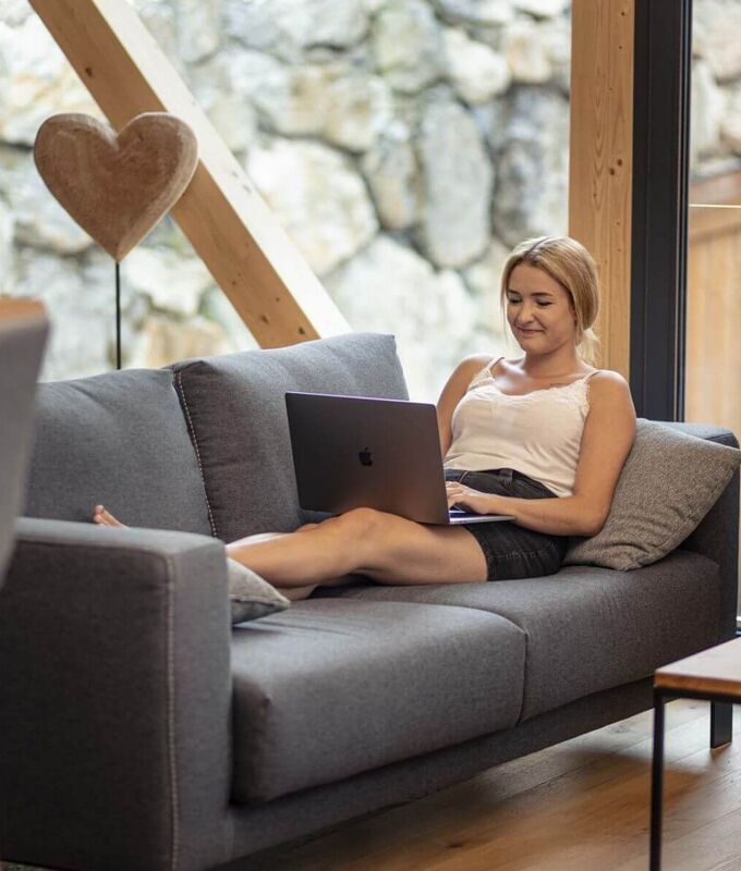 Eine junge Frau sitzt mit ihrem Laptop am Sofa.