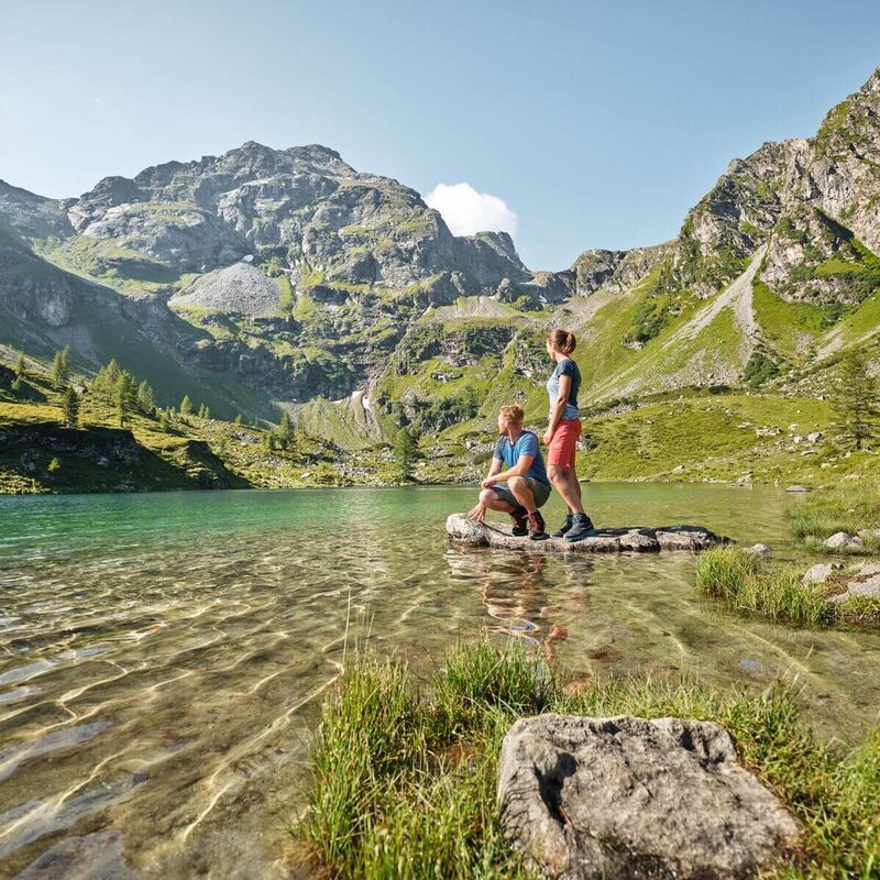 Ein Paar in sportlicher Kleidung genießt eine Auszeit an einem Bergsee mit beeindruckender Alpenkulisse