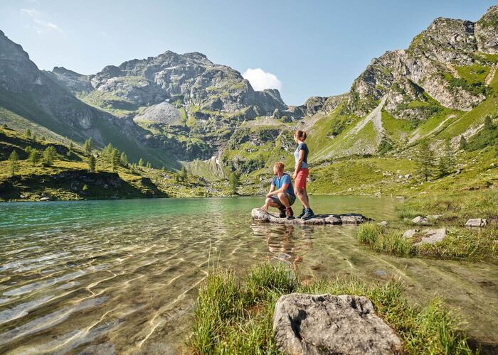 Ein Paar in sportlicher Kleidung genießt eine Auszeit an einem Bergsee mit beeindruckender Alpenkulisse