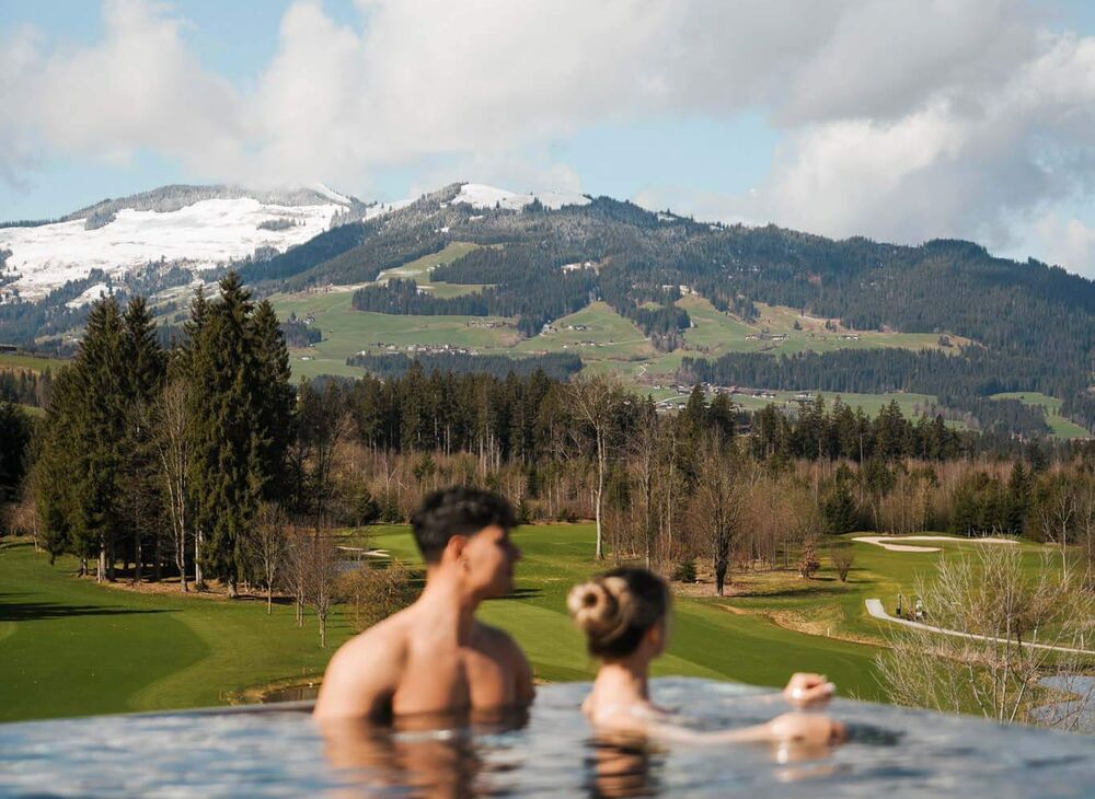 Pärchen schwimmt im Infinitypool mit Blick auf den Golfplatz und Berge