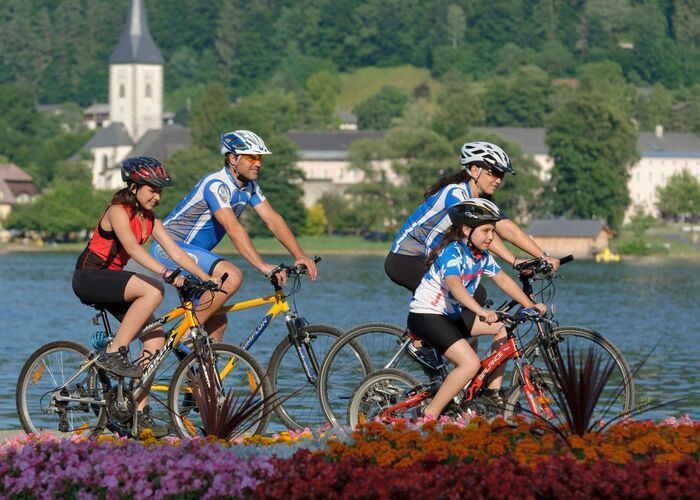 Eine Familie fährt gemütlich mit dem Fahrrad an einem See entlang und genießt die umliegende Berglandschaft in Österreich