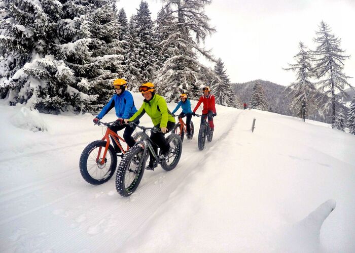 Eine Gruppe von Bikern fährt in warmer Winterkleidung mit Fatbikes und breiten Reifen eine verschneite Bergstrecke hinauf