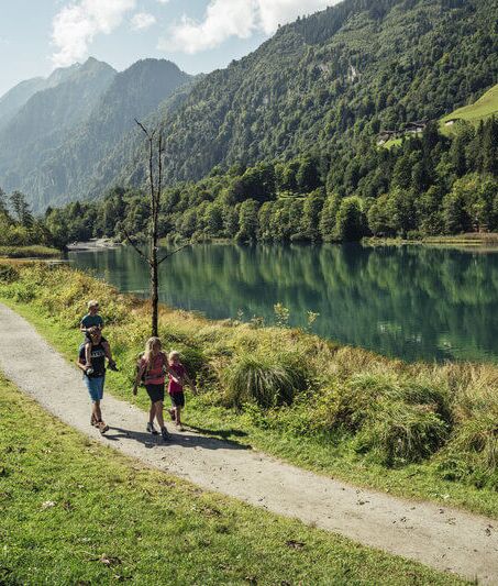 A family with two children walks around the idyllic Klammsee lake surrounded by high mountains.