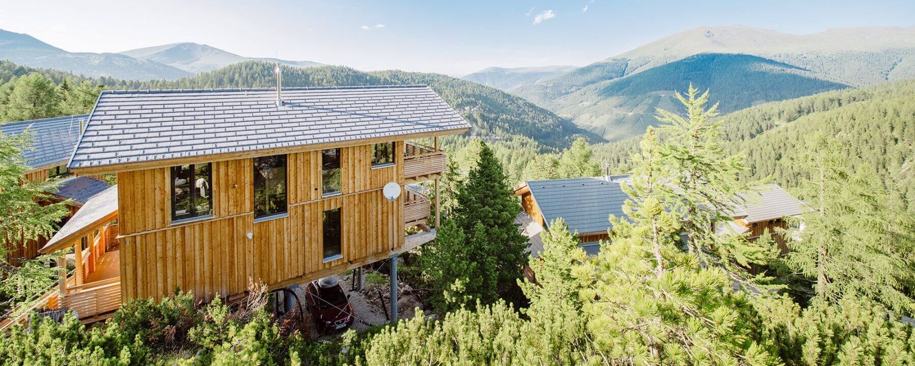 Ferienhäuser im Zirbenwald mit den Bergen im Hintergrund