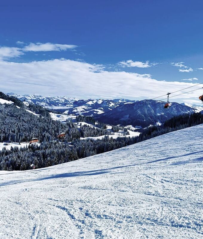 Moderne Sesselbahn schwebt über eine breite Carvingpiste.