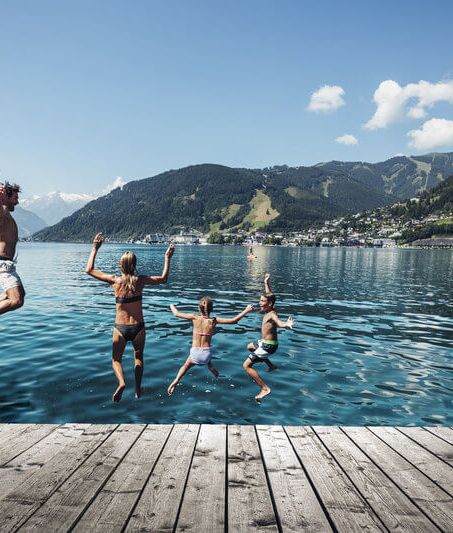 Family jumping into Lake Zell, with the Kitzsteinhorn and the town of Zell am See in the background.