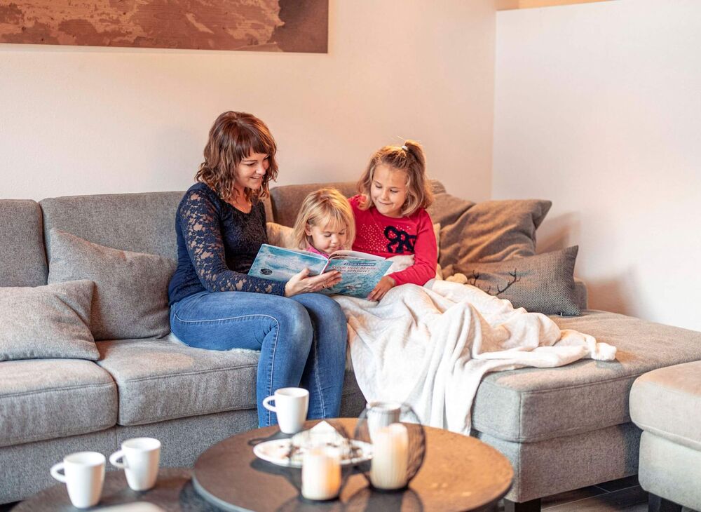 Mum reads a book on the couch with her children and everyone enjoys a hot chocolate