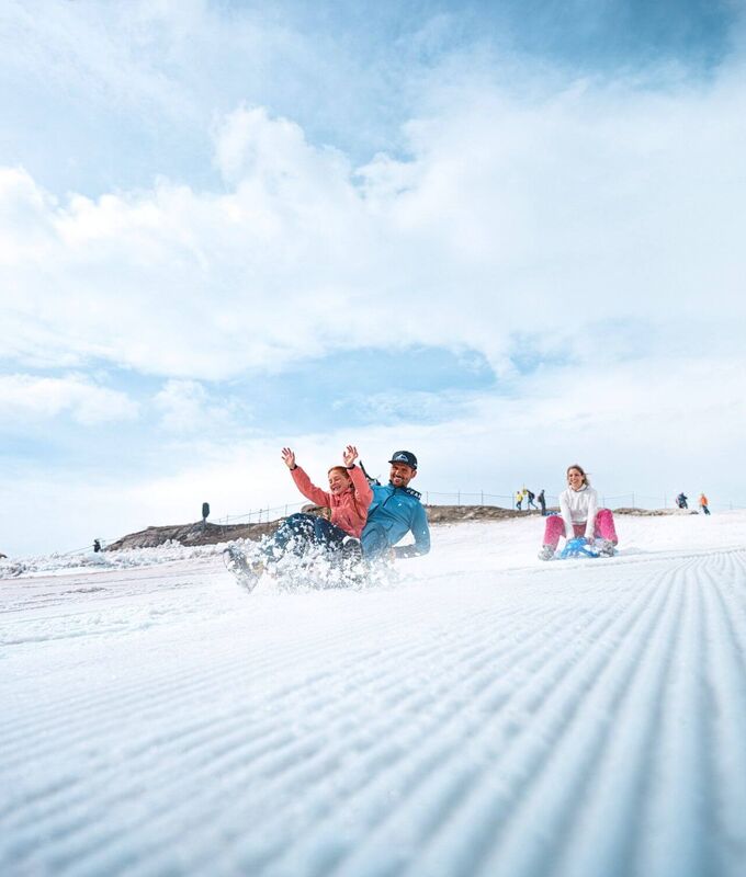 A family sliding on bobs through a groomed snowfield on the Kitzsteinhorn glacier in summer.