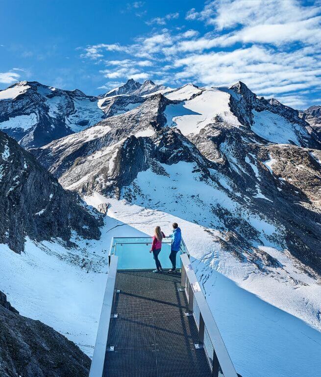 A couple looks out from a panorama platform at the Großglockner and other 3,000 metre peaks of the Hohe Tauern.