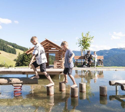 Two children balance on wooden elements in the water.