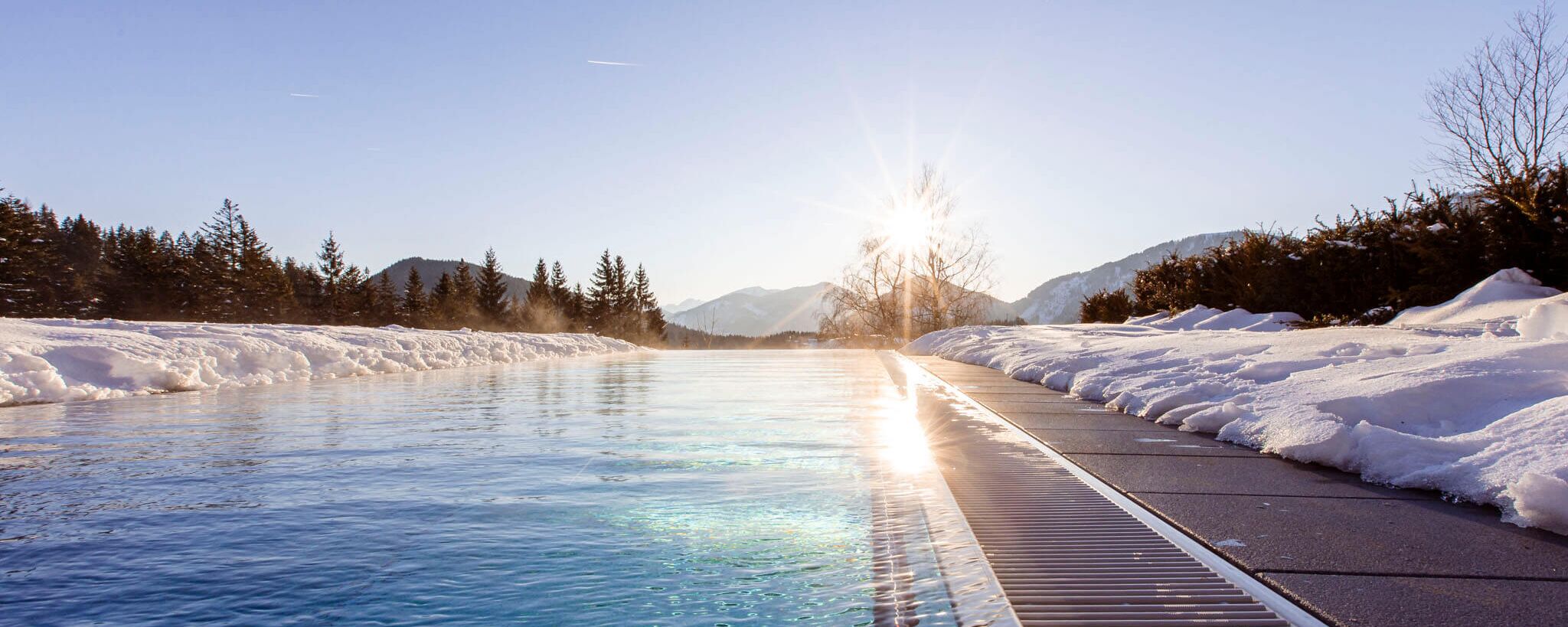 Infinitypool im Winter mit verschneiter Terrasse und Blick auf die umliegenden Wälder und Berge.