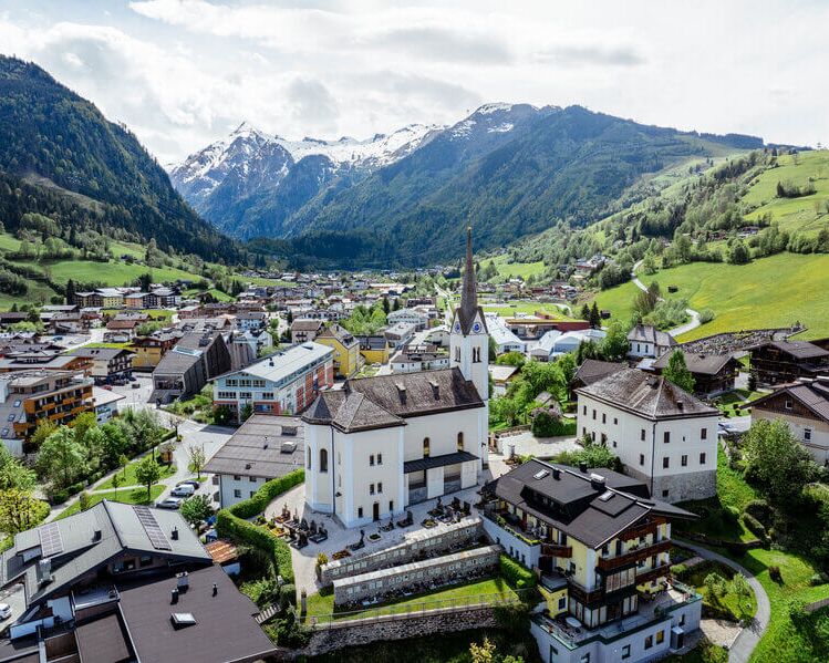 Blick von oben auf das Ortszentrum von Kaprun mit seiner Kirche, im Hintergrund das Kitzsteinhorn.