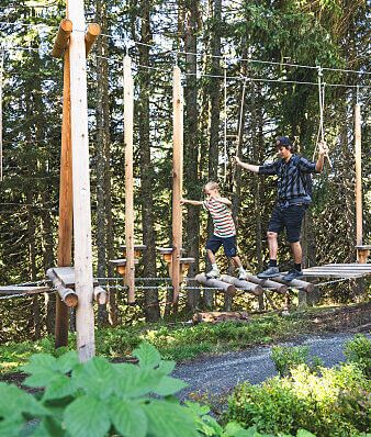 A father crosses a rope bridge in the forest with his young son.