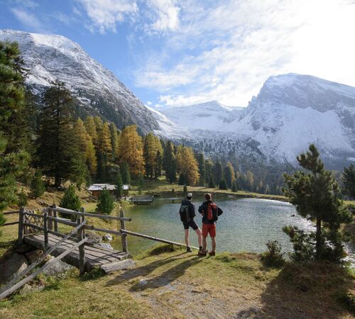 Wanderer stehen am klaren Bergsee im Zillertal, umgeben von herbstlichen Wäldern und leicht verschneiten Gipfeln