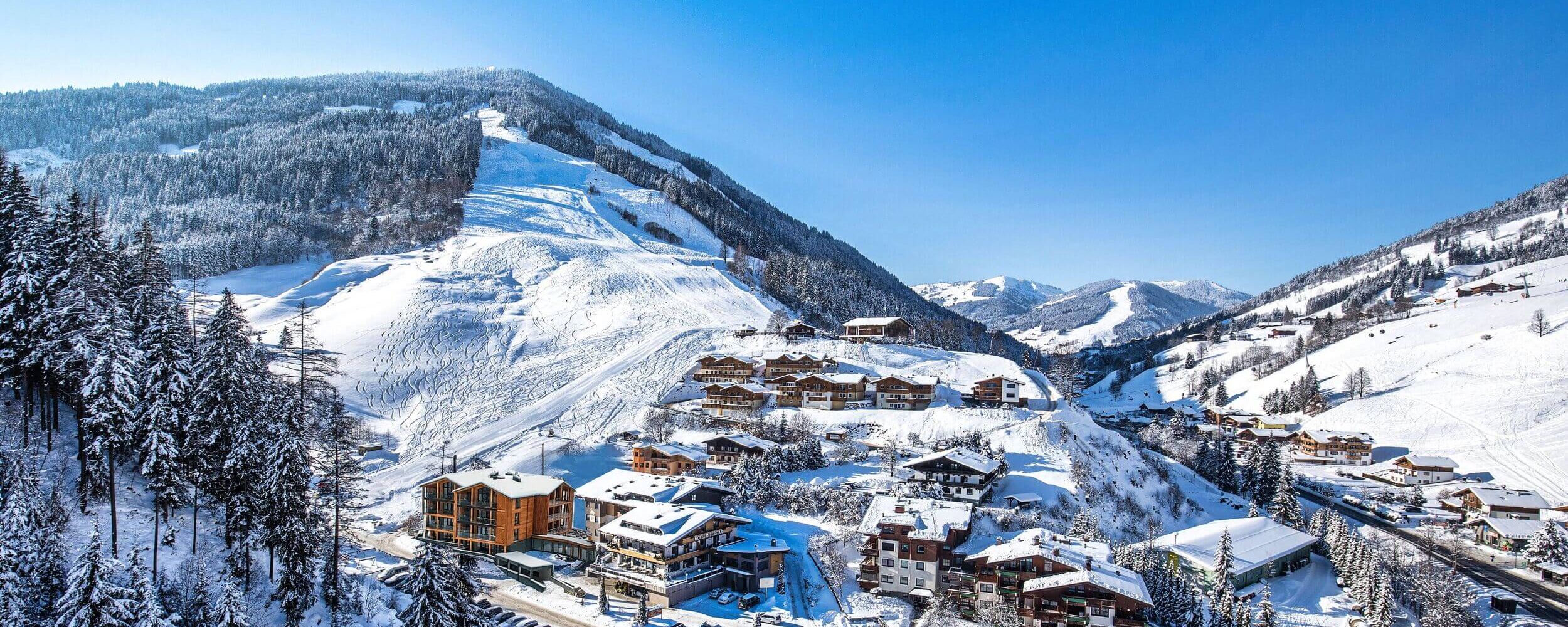 Ferienwohnungen und Häuser an einer Skipiste in Österreich mit viel Schnee und traumhaft blauem Himmel