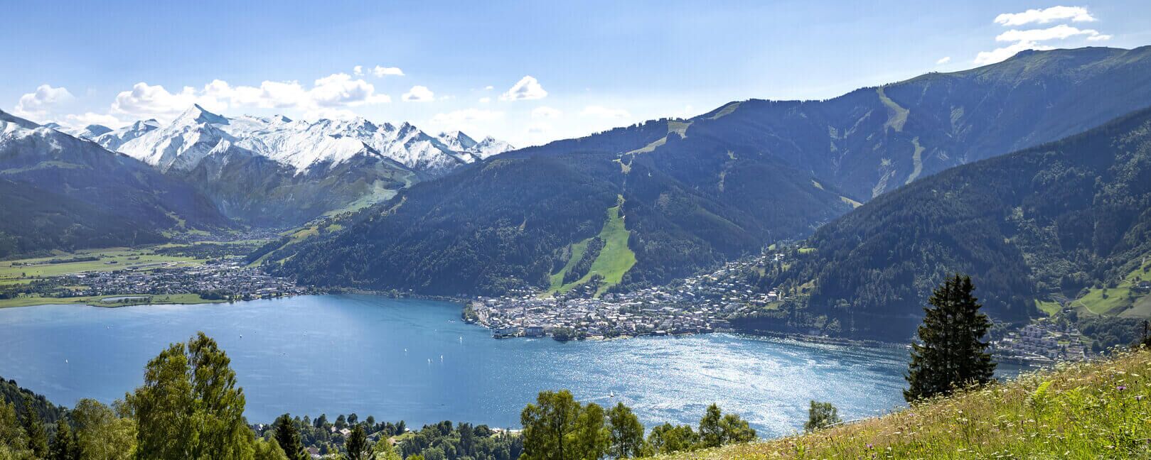 Der Zeller See eingebettet zwischen Bergen, dem Kitzsteinhorn Gletscher, blühenden Wiesen und der Stadt Zell am See.