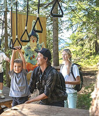 A father helps two boys navigate motor skills elements at the forest playground.
