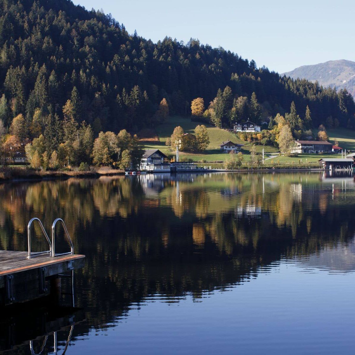 Ein stiller Bergsee in Tirol spiegelt am frühen Morgen die umliegenden Wälder und majestätischen Gipfel im klaren Wasser