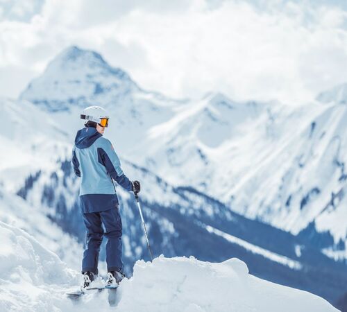 Skifahrer steht am Pistenrand im Tiefschnee und genießt den Ausblick auf die verschneiten Berge und Täler