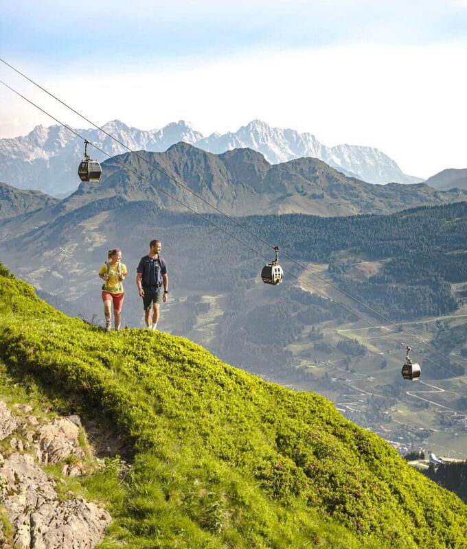 Über 2 Wanderern fährt die Sommerbergbahn, im Hintergrund 2 imposante Bergkämme.