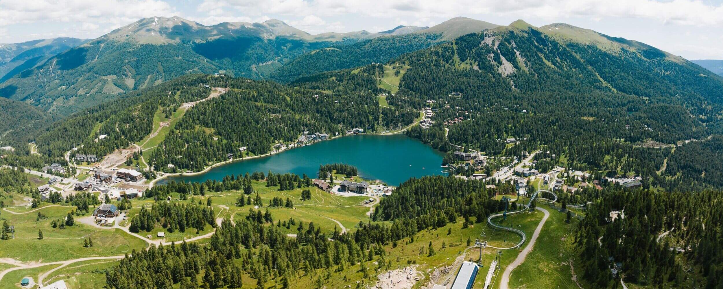 Luftaufnahme des Turracher Sees in Kärnten im Sommer – klare Bergluft, tiefblaues Wasser und umgebende Wälder auf der Turracher Höhe