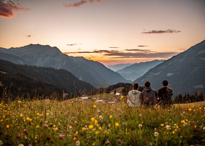 Urlauber entspannen auf einer Almwiese und genießen die besondere Lichtstimmung der Abenddämmerung inmitten imposanter Berglandschaft