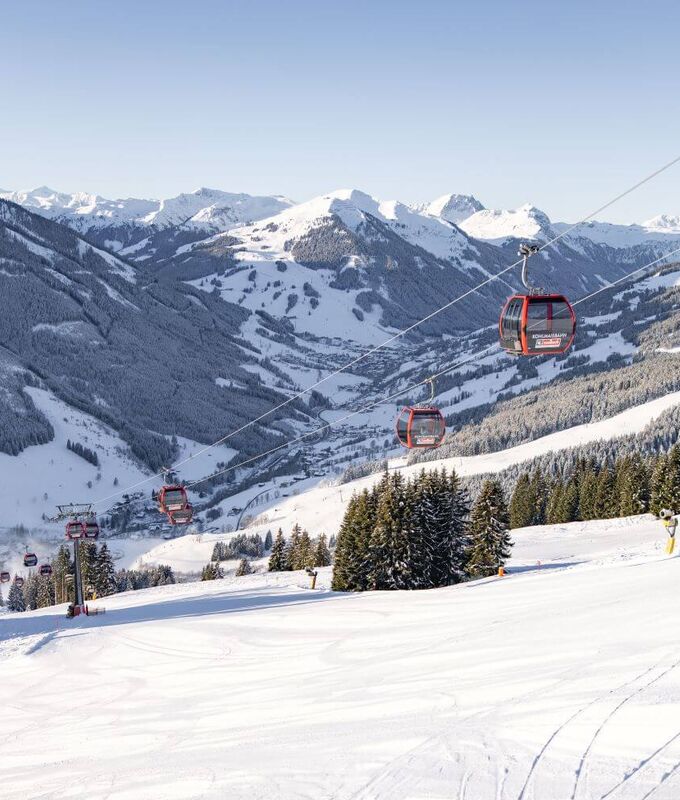 Kohlmaisbahn gondola lift with freshly groomed piste, with the snow covered Glemmtal valley in the background.