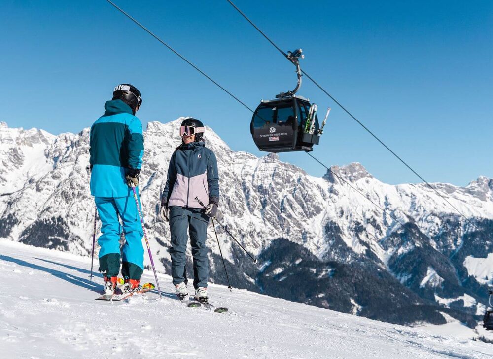 2 skiers are standing below the Leogang Steinberg cable car.