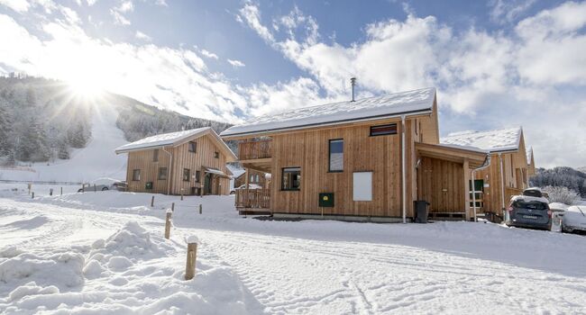 Sonniger Wintertag mit Ferienhäusern, Skipiste und viel Schnee