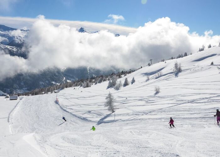 Familie beim Skifahren auf einer breiten Piste mit Neuschnee