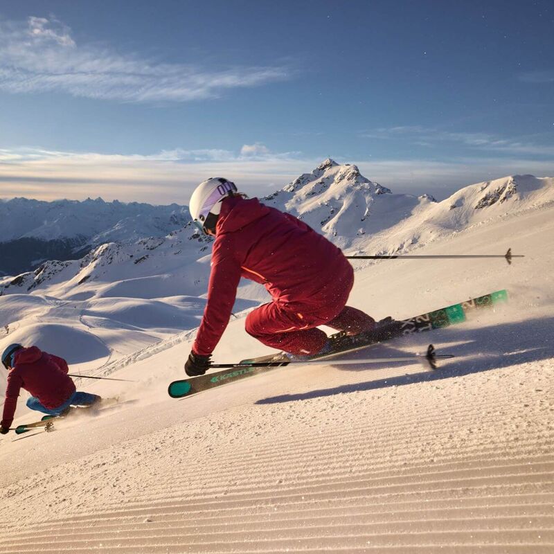 2 skiers carve down a long descent on the freshly groomed piste in the Silvretta-Montafon ski area.