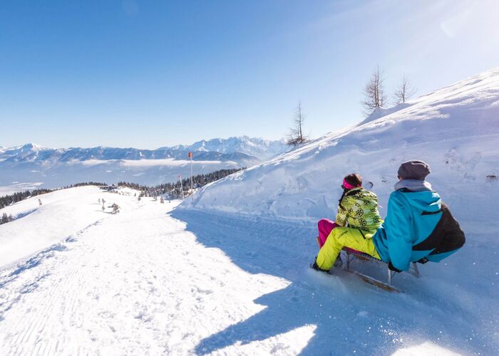 Person beim Rodeln im verschneiten Naturpark Dobratsch in der Region Villach