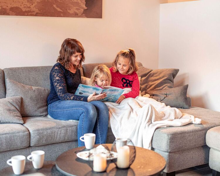 Mum reads a book on the couch with her children and everyone enjoys a hot chocolate