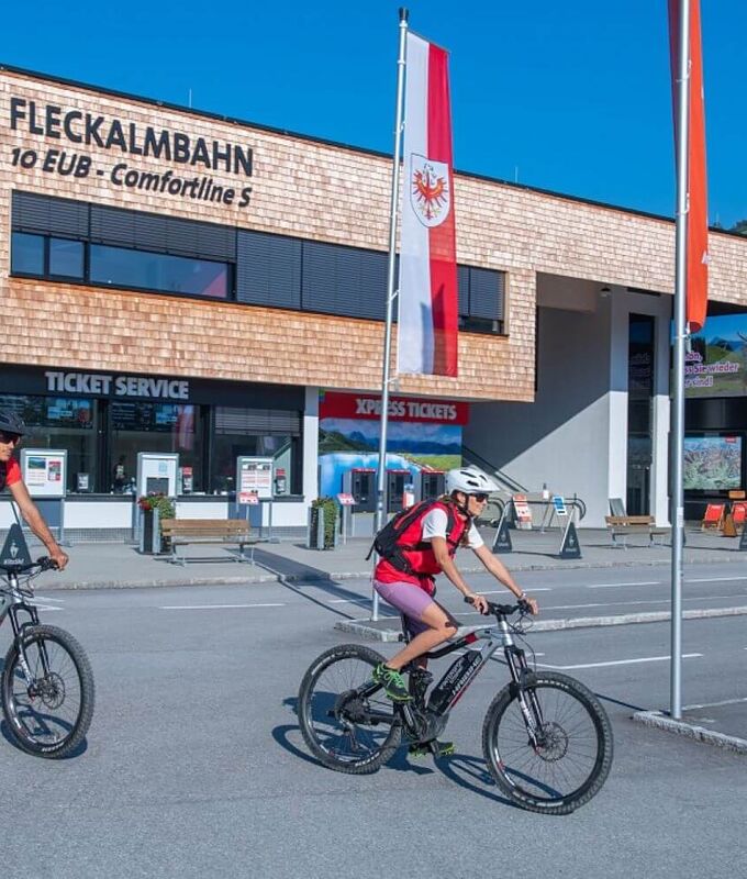 2 E Biker radeln zur Talstation einer Sommerbergbahn.