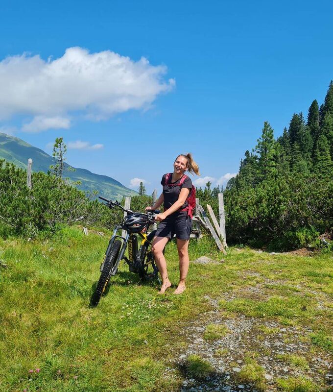 Bikerin in den Kitzbüheler Alpen schiebt ihr E Bike ein Stück barfuß.