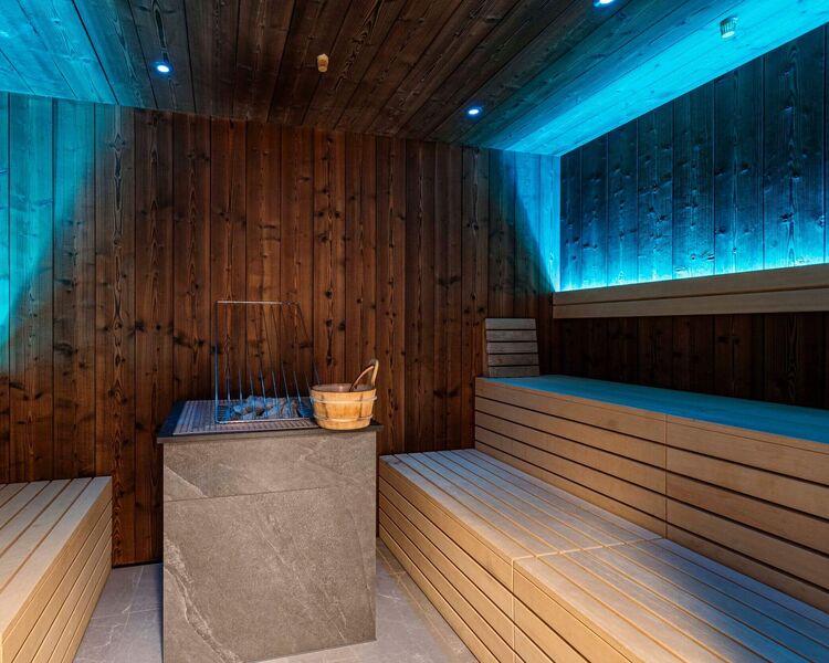Sauna with cosy wooden benches, stone sauna heater and relaxing lighting by ALPS RESORTS