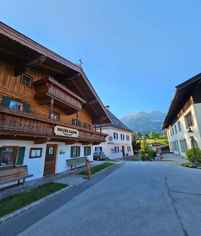 Goinger Dorfplatz mit altem Bauernhaus und Blick auf den Wilden Kaiser.