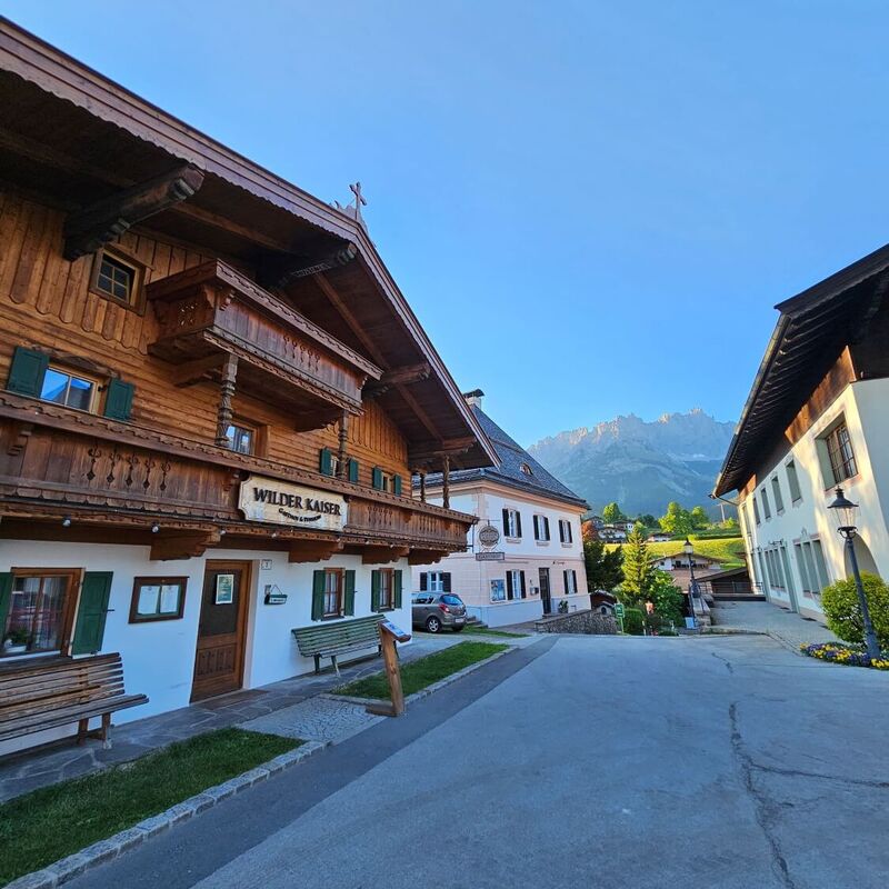 Goinger Dorfplatz mit altem Bauernhaus und Blick auf den Wilden Kaiser.