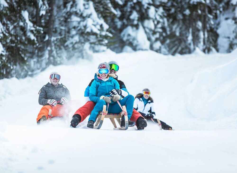 Group of friends tobogganing in the snowy forest