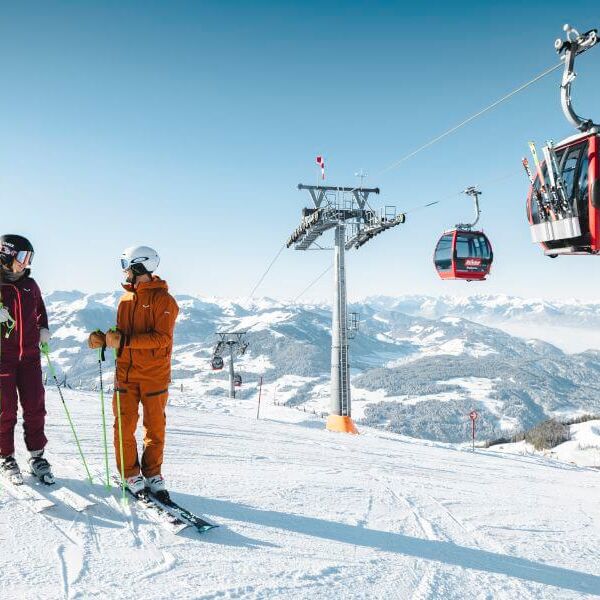 Two skiers are standing on the slope below a cable car.
